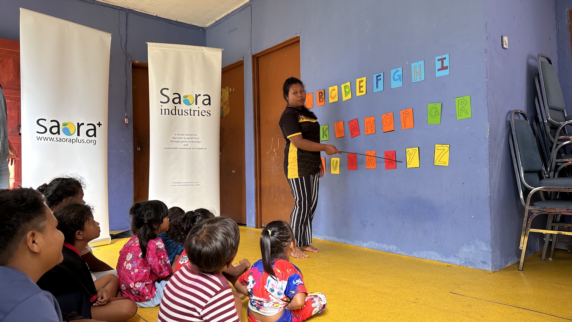 Orang Asli children studying at desks inside a Saora+ learning centre, with a trained village educator guiding them